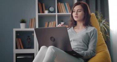 Çanta koltuğunda otururken dizüstü bilgisayarda çalışan düşünceli bir kız.