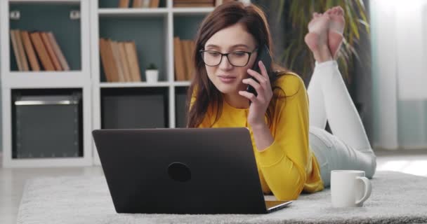 Vrouw praten over de telefoon terwijl liggend op de vloer met de computer — Stockvideo