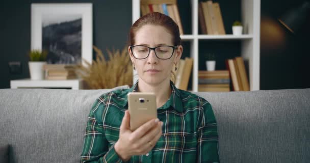 Gözlüklü güzel kadın evde akıllı telefon kullanıyor. — Stok video