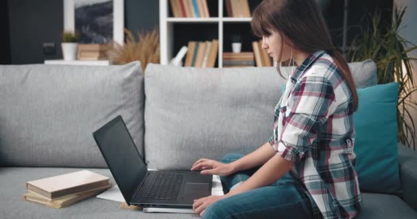 Söt flicka sitter på soffan och skriver på laptop — Stockvideo