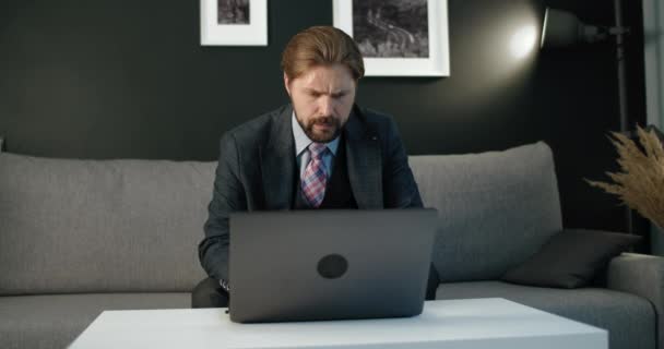 Бородатый мужчина сидит на диване и использует беспроводной ноутбук — стоковое видео