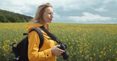 Olgun bir kadın tarlada yürüyor ve fotoğraf çekiyor.