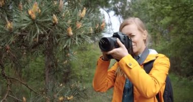 Yeşil ormanda çam ağaçlarının fotoğraflarını çeken neşeli bir kadın.