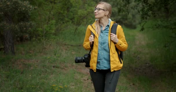 Kobieta spacerująca po lesie z aparatem cyfrowym i plecakiem — Wideo stockowe