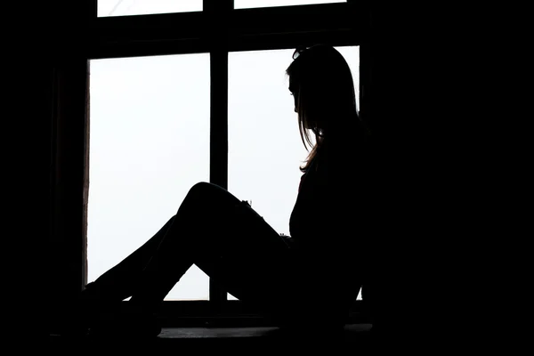 Woman looking through window sitting on the window sill — Stock Photo, Image