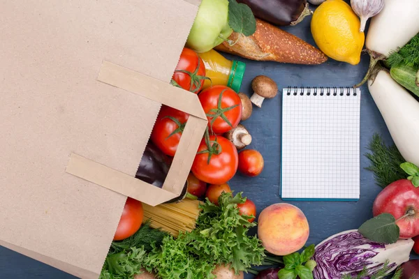 Бумажный пакет с продуктами питания и ноутбуком с пустой страницей — стоковое фото