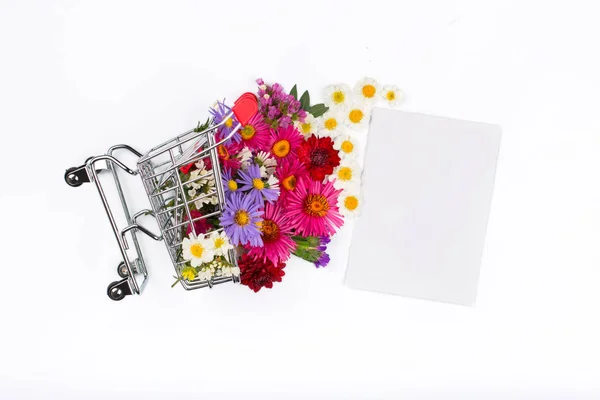 Carrito de compras con diferentes flores silvestres y tarjeta en blanco — Foto de Stock