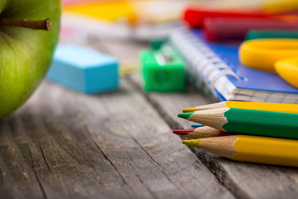 Colored pencils with school supplies and green apple