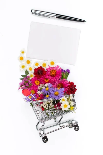 Carrito de compras con diferentes flores silvestres y tarjeta en blanco — Foto de Stock