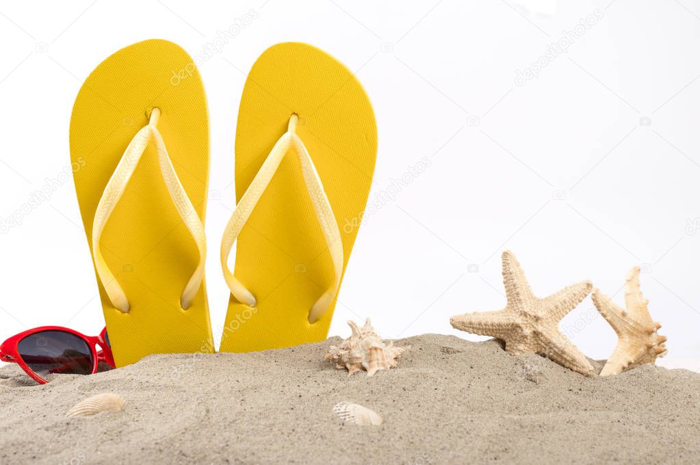Beach slippers with sunglasses, shells and starfish in the sand