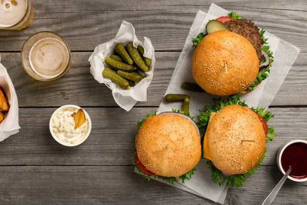 Hamburgery i kanapka na drewnianym stole z sosami i piwo — Zdjęcie stockowe