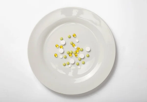 Diferentes pastillas en un plato blanco sobre un fondo blanco — Foto de Stock