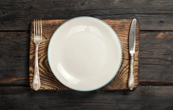 Assiette vide avec fourchette et couteau sur fond bois foncé — Photo