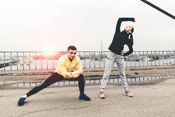 Pareja de jóvenes atletas en ropa deportiva están entrenando en el puente de la ciudad — Foto de Stock