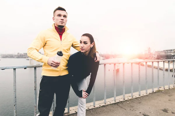 Couple young athletes in sports clothing standingg on city bridg