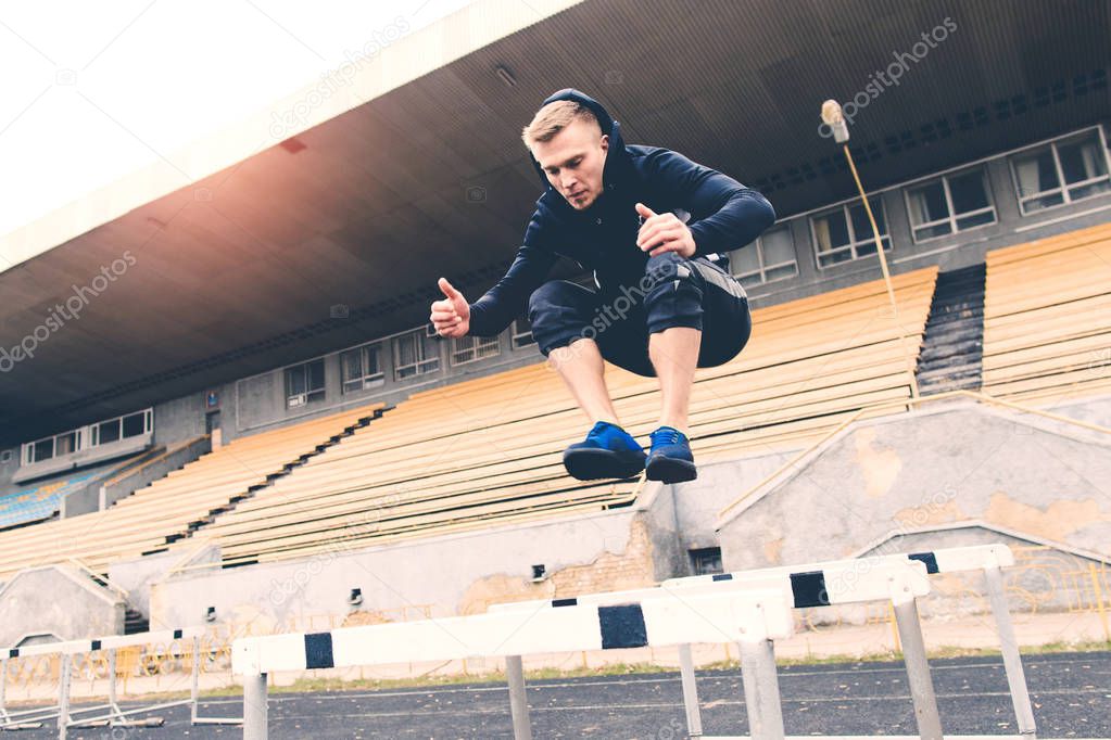 Young athlete jumping over hurdle during workout at the stadium