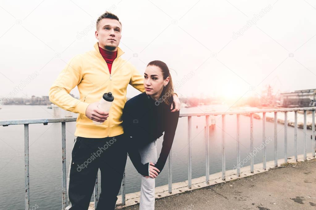 Couple young athletes in sports clothing standingg on city bridg