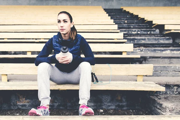 Mujer joven en ropa deportiva sentada en el viejo estadio — Foto de Stock