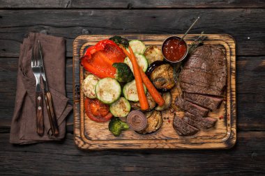 Ahşap masa üzerinde ızgara sebzeli biftek dilimlenmiş