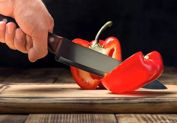 Man's hand with a kitchen knife cuts red pepper — Stock Photo, Image