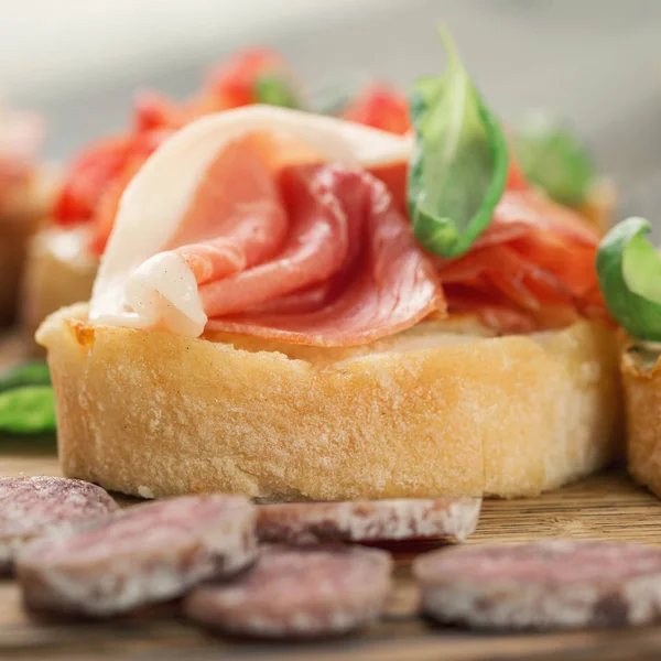 Bruschetta with prosciutto and basil on a wooden table — Stock Photo, Image