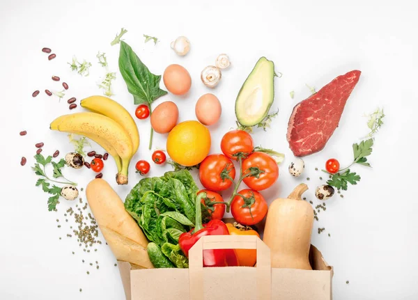 Saco de papel completo de diferentes alimentos saudáveis no fundo branco — Fotografia de Stock