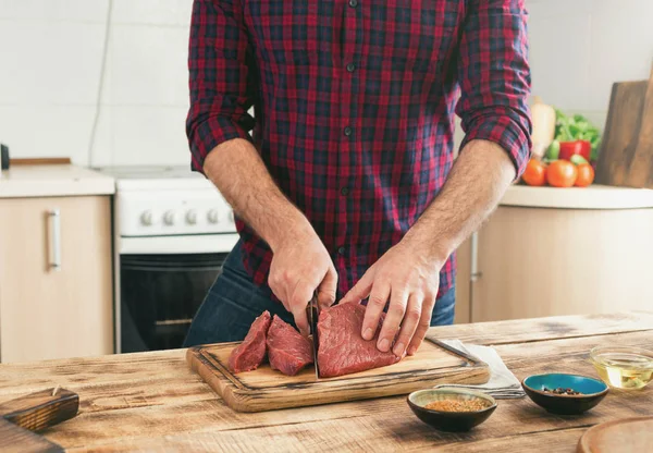 Man cooking beef meat on wooden table in the kitchen — Stock Photo, Image