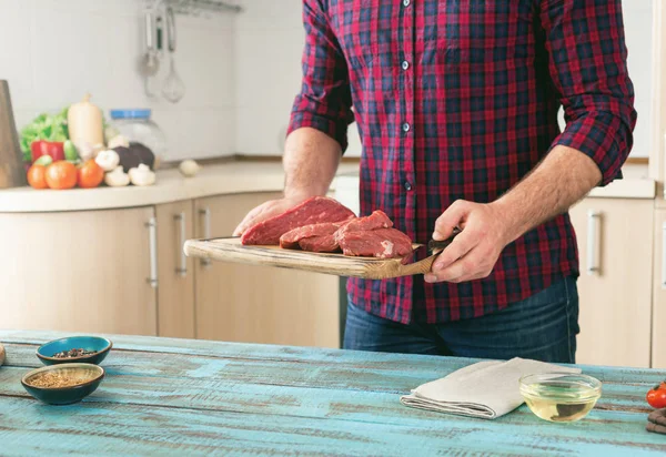 Homem cozinhar carne na mesa de madeira na cozinha da casa — Fotografia de Stock