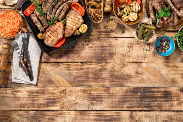 Diferentes alimentos cozidos na grelha na mesa de madeira — Fotografia de Stock