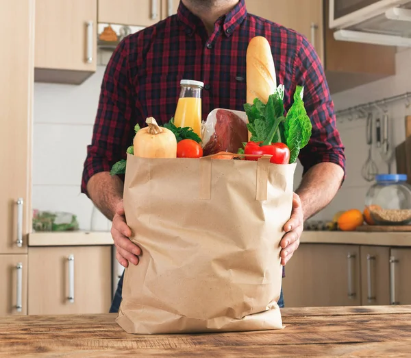 Man met papieren zak van gezonde voeding op houten tafel — Stockfoto