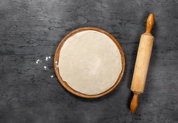 Тесто для пиццы на круглой деревянной доске со скалкой — стоковое фото