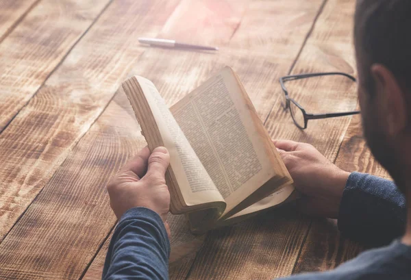 Uomo che legge libro seduto a un tavolo di legno — Foto Stock