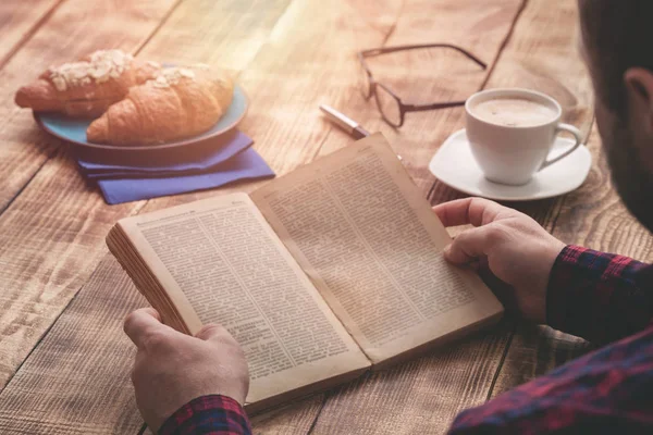 Ο άνθρωπος τρώει πρωινό και διαβάζοντας το βιβλίο εσωτερικη — Φωτογραφία Αρχείου