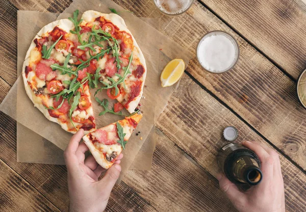 Homem come pizza com cerveja leve na mesa de madeira — Fotografia de Stock