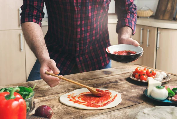 Человек готовит домашнюю пиццу на деревянном столе — стоковое фото