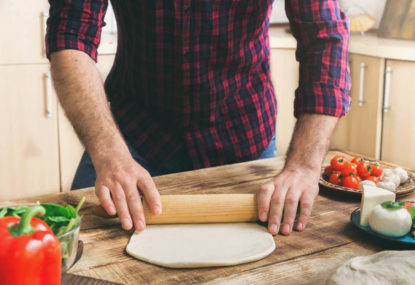 Человек выкатывает тесто для приготовления домашней пиццы — стоковое фото
