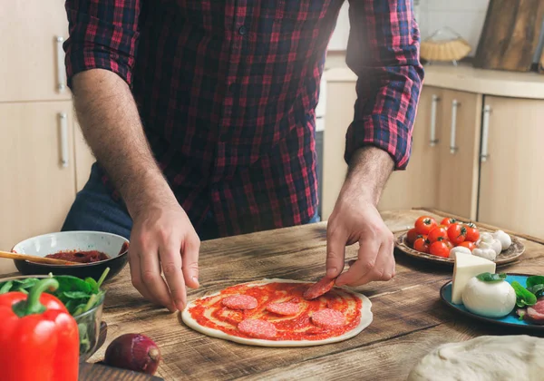 Mann bereitet hausgemachte Pizza auf Holztisch zu — Stockfoto