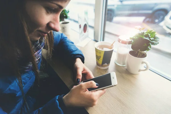 Chica se sienta en la cafetería y utiliza el teléfono móvil para comunicarse — Foto de Stock