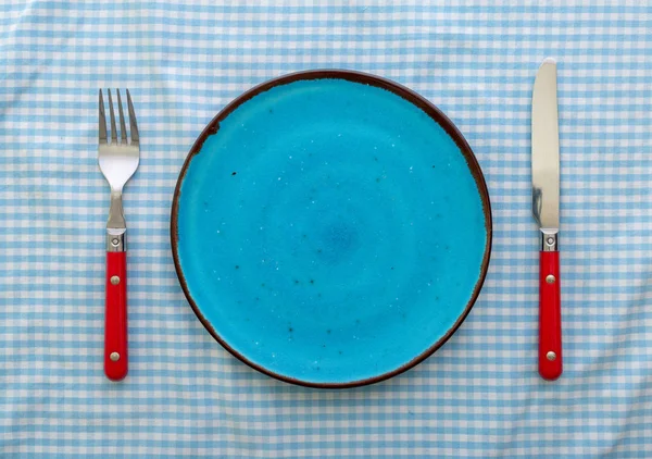 Пустая голубая керамическая плита с ножом и вилкой — стоковое фото