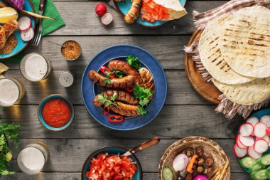 Yemek masası ile ızgara sosis, tortilla, bira ve farklı 