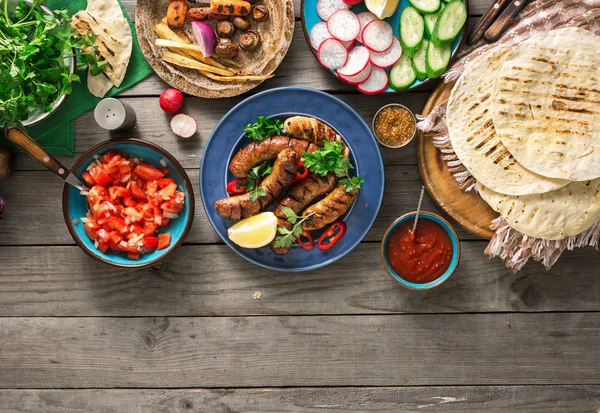 Mesa de cena con salchichas a la parrilla, envolturas de tortilla y diferentes — Foto de Stock