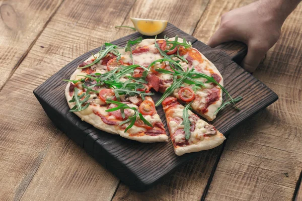 Mano maschile tiene una tavola di legno con pizza italiana — Foto Stock