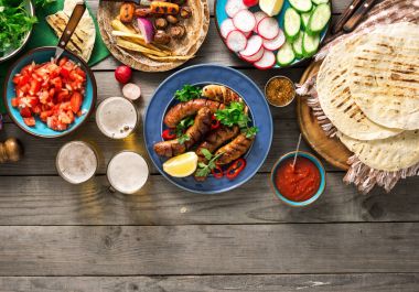 Yemek masası ile ızgara sosis, tortilla, bira ve farklı 