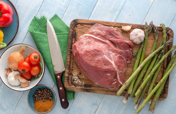 Raw meat beef on blue wooden table with different vegetables — Stock Photo, Image