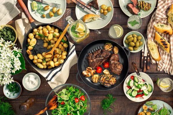 Table à manger avec gril à viande, pommes de terre rôties, aliments différents — Photo