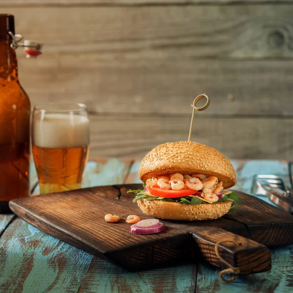 Burger mit gegrillten Garnelen auf Holztisch mit Pils — Stockfoto