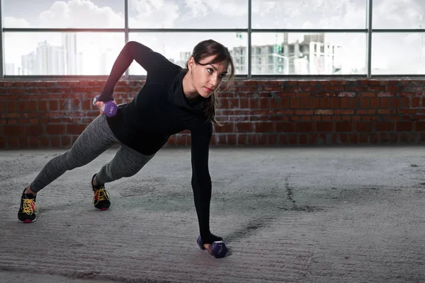Женщина-атлет отжимается с гантелями на полу — стоковое фото