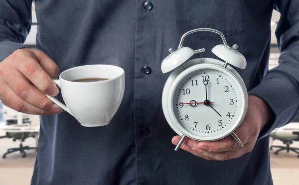 El oficinista sostiene una taza de café y un despertador — Foto de Stock