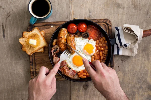 Мужчина ест английский завтрак на деревянном светлом столе — стоковое фото
