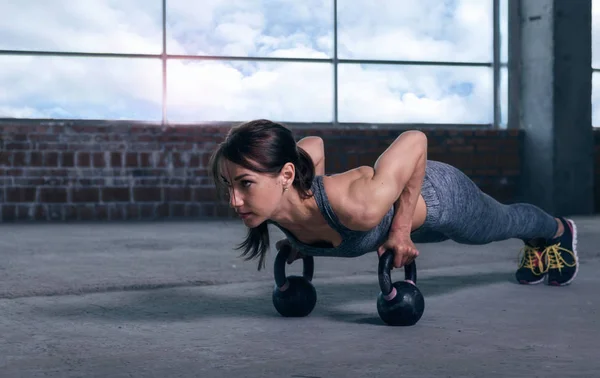 Young woman athlete in sportswear push ups with dumbbells — Stock Photo, Image